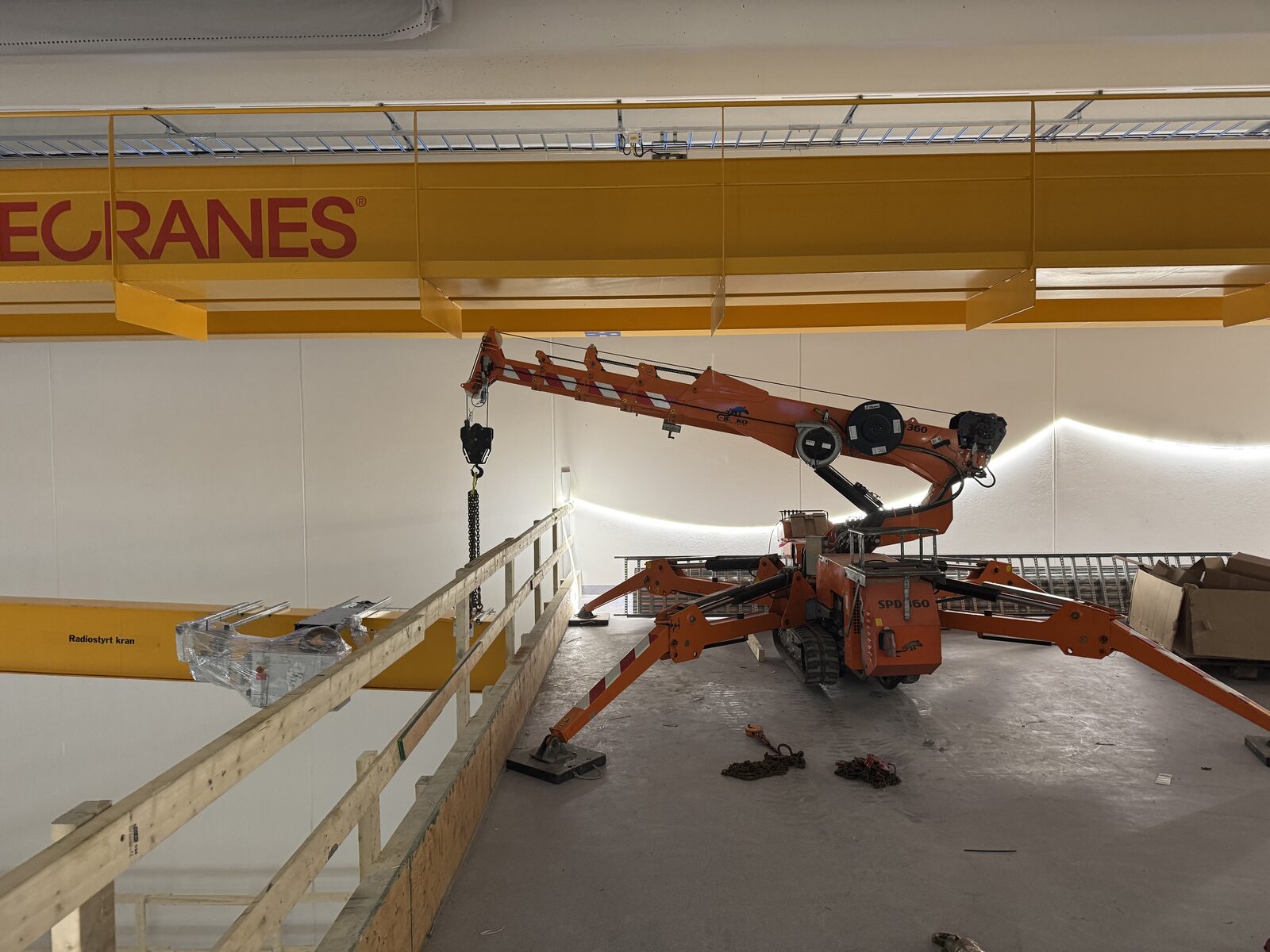Oransje spider-kran i drift inne i industribygg